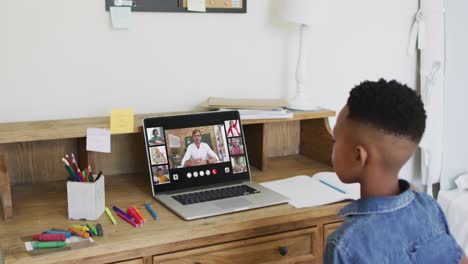 Schoolboy-using-laptop-for-online-lesson-at-home,-with-diverse-teacher-and-class-on-screen