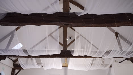 Rustic-wooden-beams-adorned-with-draped-white-fabric-in-a-ceiling-decor