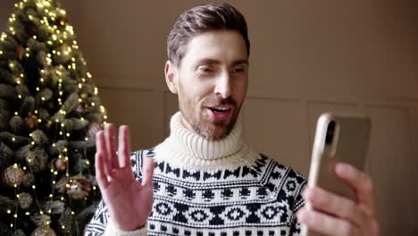 Close-Up-Portrait-Of-Happy-Male-In-Good-Mood-Videochatting-On-Cellphone-Near-Glowing-Decorated-Xmas-Tree