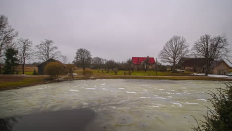 frozen lake melting surrounded by lakefront house along rural countryside throughout the day