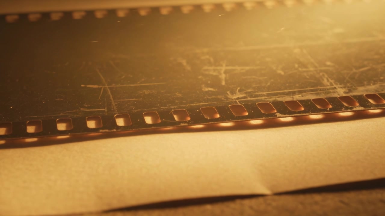 Striscia di pellicola 35mm scintillante che mostra graffi e perforazioni su un foglio sul banco, mentre una lampada calda pulsa per l'analisi.