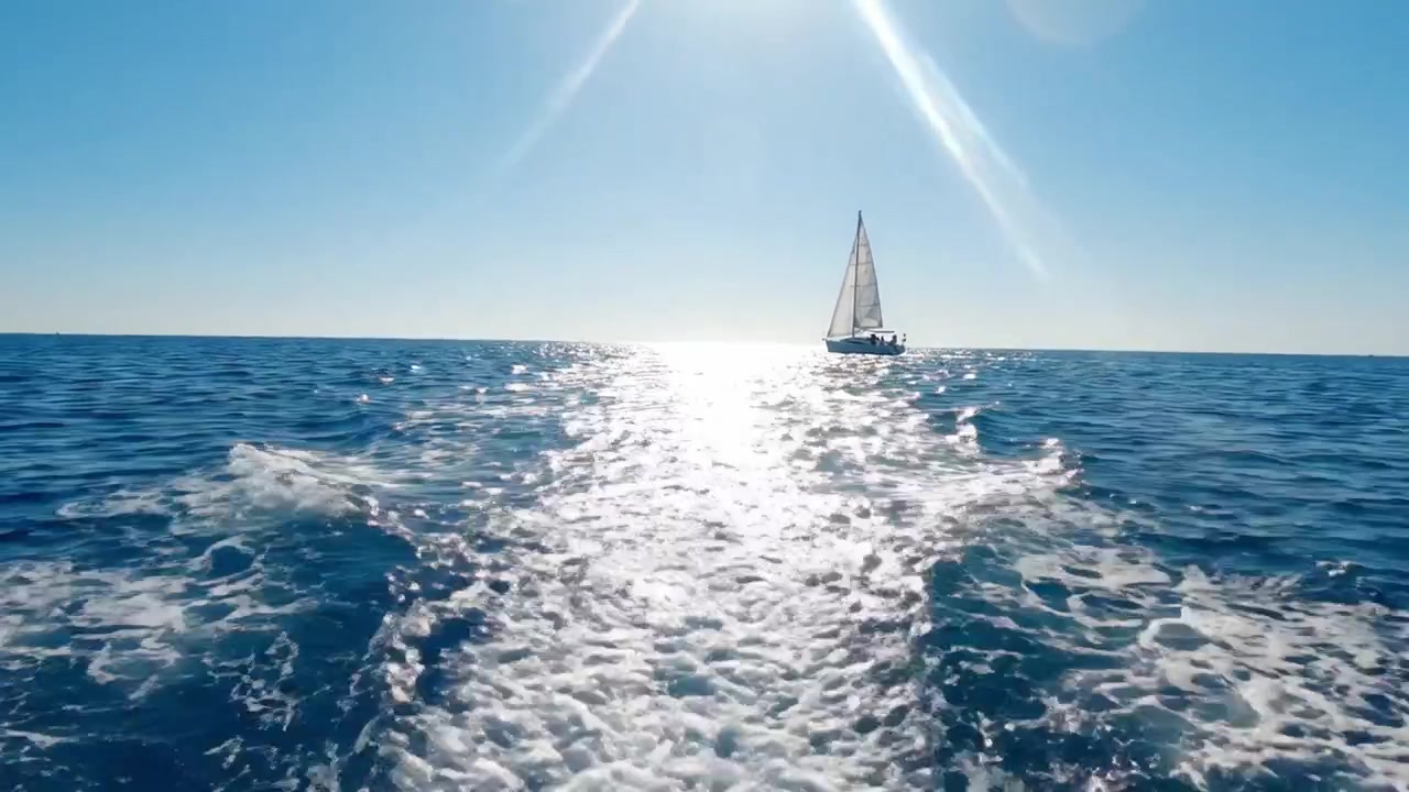 陽光が降り注ぐ海を横断する穏やかなセーリングの旅：クリスタルブルーの魅惑的な海の眺めと、海を滑るように進む優雅なヨット