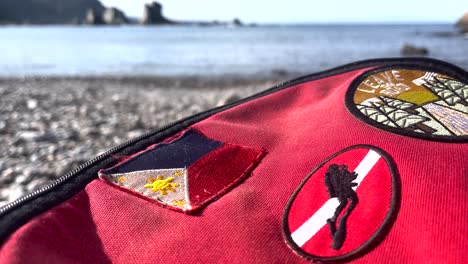 Bolso-Estilo-Eastpack-Rojo-Con-Parche-De-Bandera-De-Buceo,-Bandera-De-Filipinas-Junto-Al-Mar