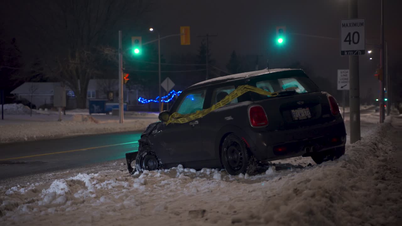 Aftermath of car accident MVA motor vehicle accident on snowy night in winter with small car wrapped in yellow caution tape with traffic lights and street lights in background