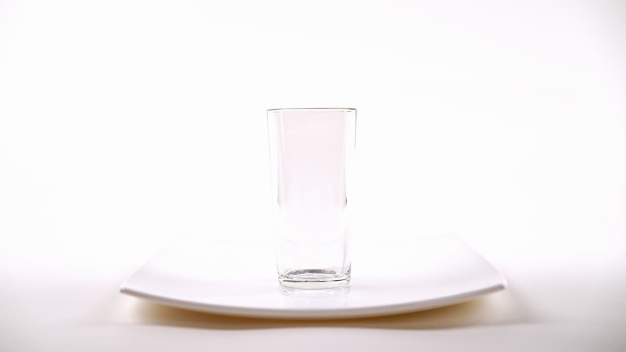 рука погружает чайный мешок в прозрачный стакан воды на белой тарелке, белый фон