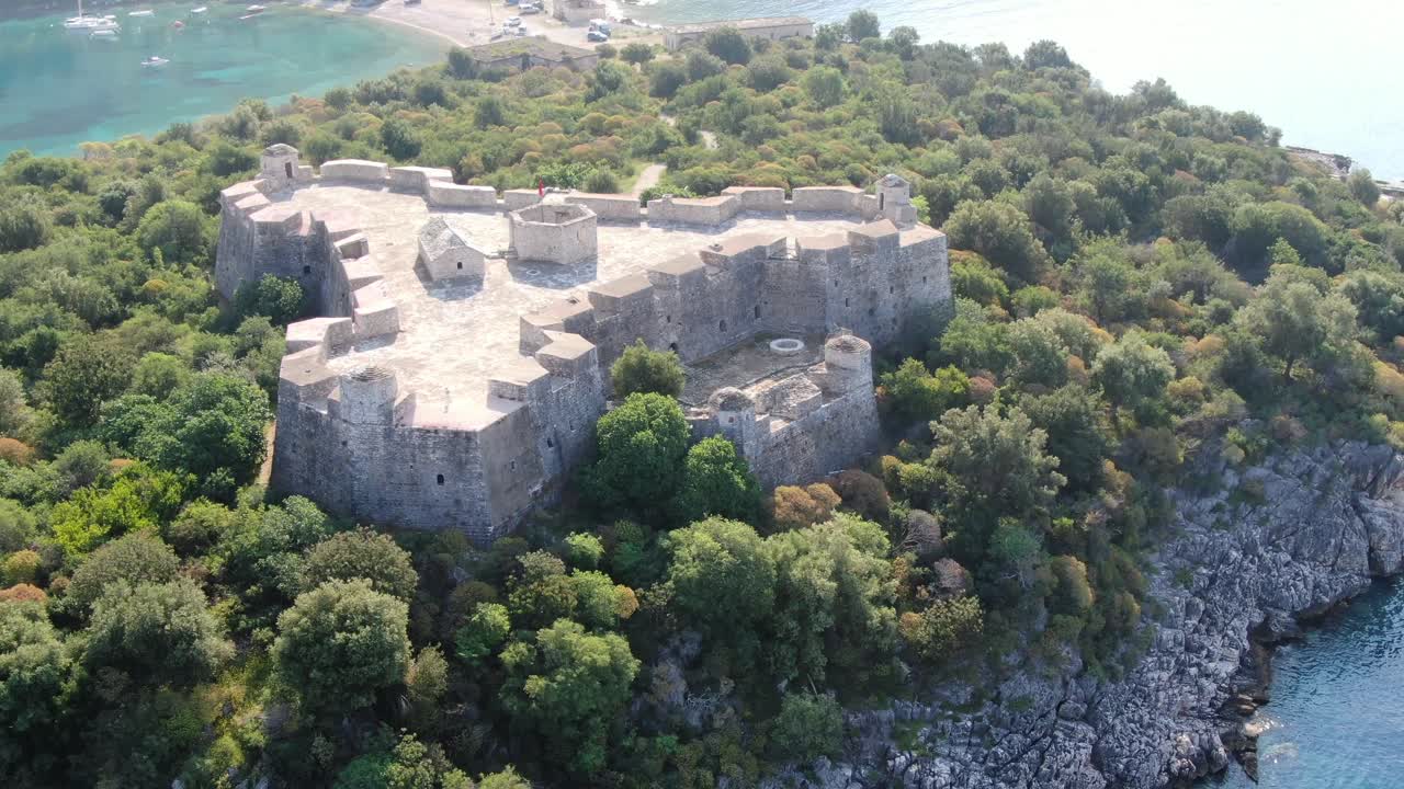 Vista drone in Albania che sorvola un forte medievale su un'isola verde sopra un oceano blu e limpido in una giornata di sole