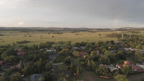 4k-Aéreo,-Volando-Sobre-Un-Paisaje-Urbano-De-Casas-Residenciales,-Avanzando-Hacia-Un-Campo-Abierto-Con-Un-Toque-De-Arco-Iris-En-El-Cielo,-Centurión,-Sudáfrica