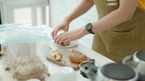 man cutting with a knife crusty artisan bread in the backery kitchen, bread buns are stored in plastic bags