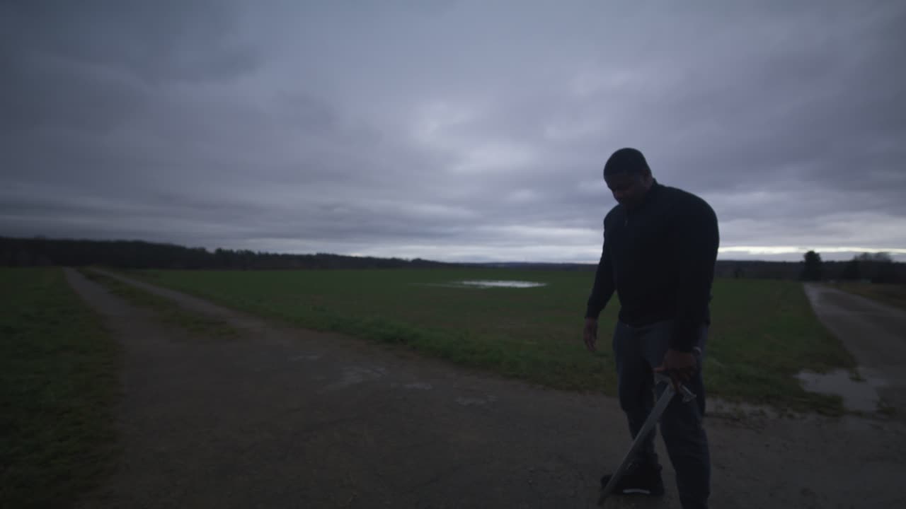 moderno espadachín negro guerrero esperando a su oponente en el campo abierto bajo el cielo gris, europa, 4k | musculoso, intimidante, sombra, figura, borroso, ropa oscura, poderoso, cansado, bombeado, postura