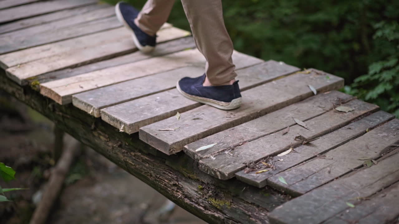 Man take walk on wooden bridge. Man legs on old wooden bridge through small river