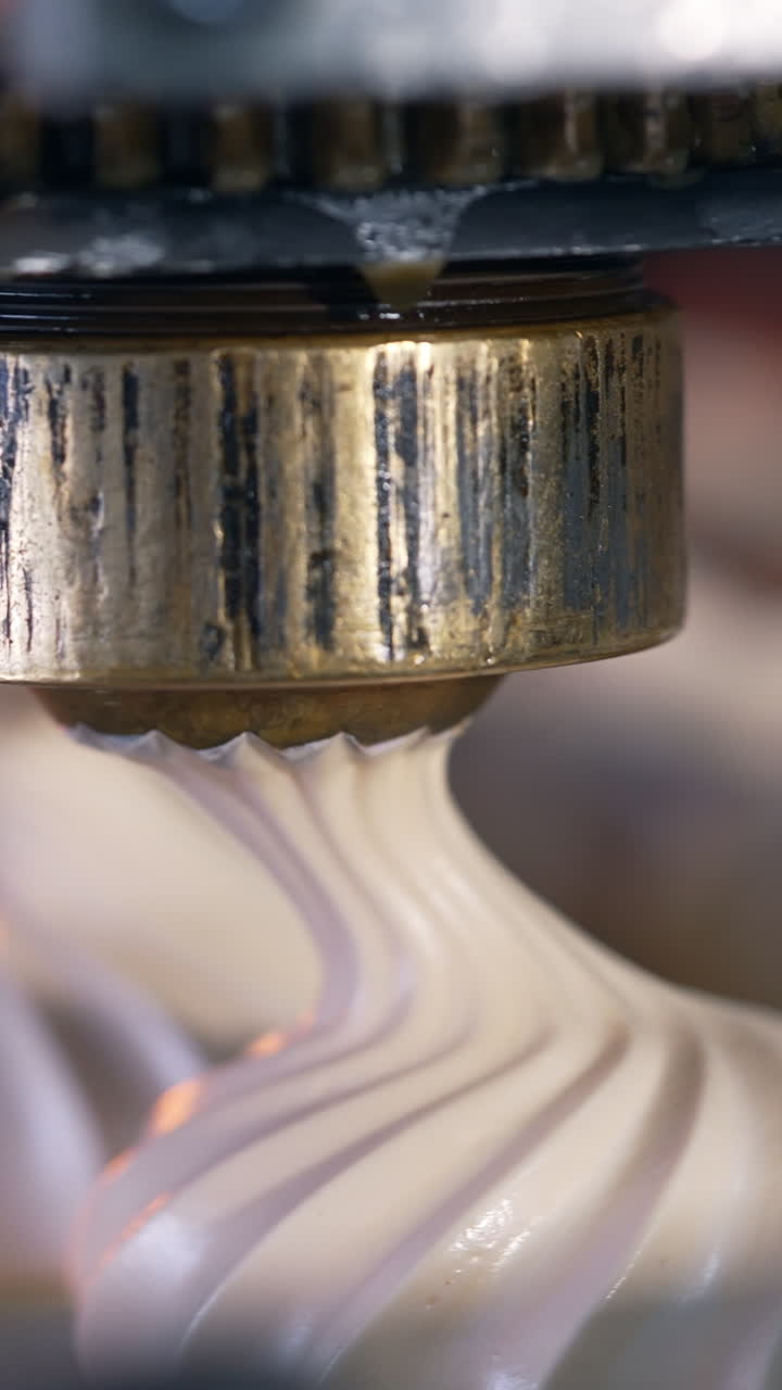 Round metal nozzles of automated machine deposit marshmallows on conveyor belt. Close up. Blurred backdrop. Vertical video