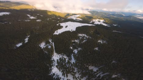 fpv drone shot captured in slovenia in pokljuka forest with surrounding nature and mountains at golden hour at sunset with fast and cinematic movement from over the clouds to the village