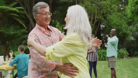 Animation-of-happy-caucasian-senior-couple-danging-in-garden-while-having-lunch-with-friends