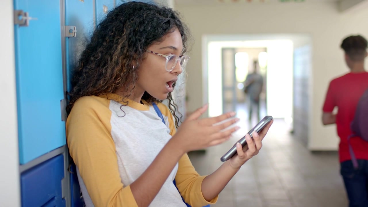 Adolescente appoggiato agli armadietti della scuola che scorre il telefono, causando un effetto visivo verde acqua che si concentra sullo schermo del telefono che reagisce