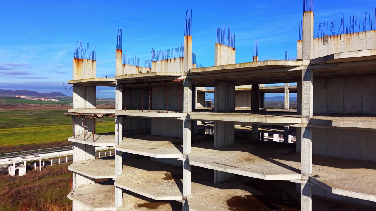 Verlaten betonnen gebouwkelet met blootliggend wapeningsstaal, Pomorie, Bulgarije. Luchtfoto met drone toont roestige kolommen, open verdiepingen en groene velden onder een blauwe lucht.