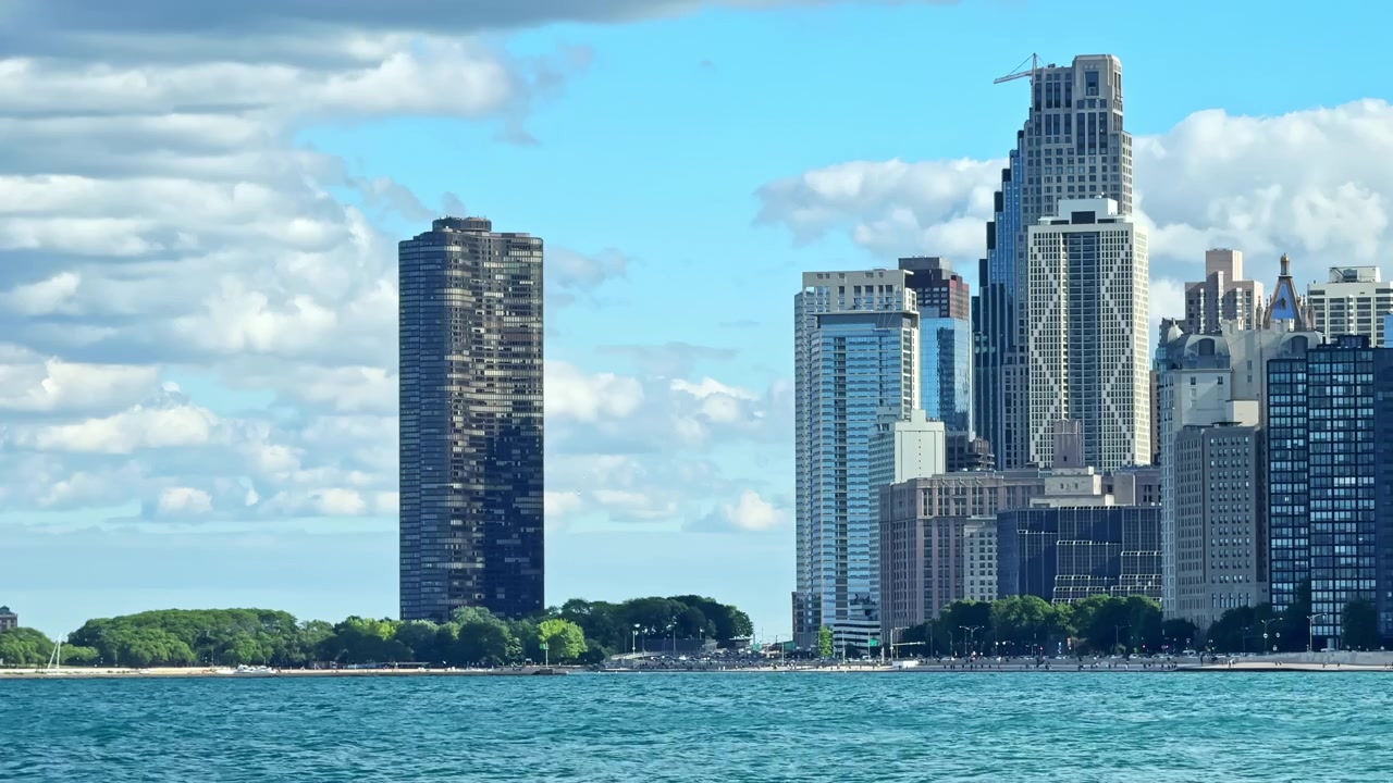 Edifícios se erguem ao longo da margem de um lago em Chicago, mostrando o horizonte sob um céu azul com algumas nuvens ao fundo.