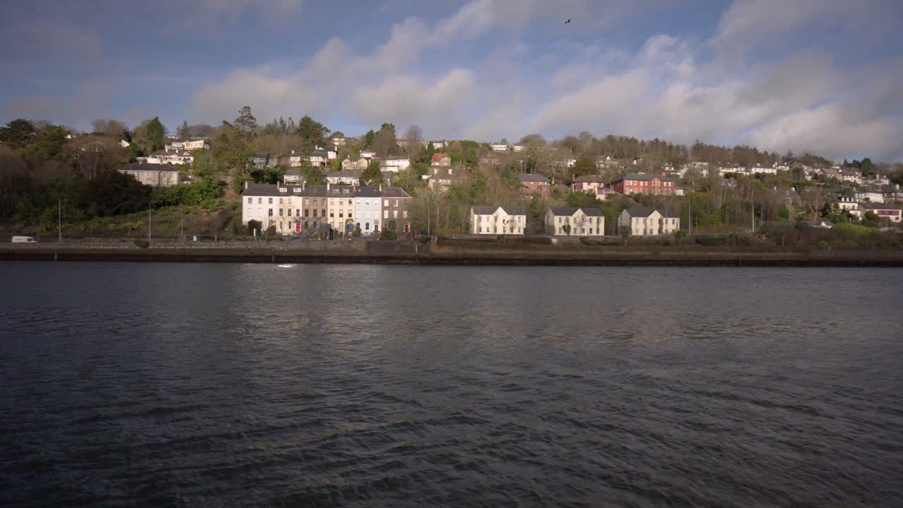 아일랜드의 화창한 날 배경에 자동차가 지나가는 집들이 있는 도시 환경에서 강과 풍경의 팬 샷