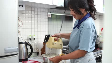 joven asiática mezclando masa para hornear usando un mezclador eléctrico en la cocina