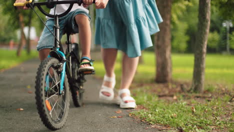 a low-angle view of a child riding a bicycle, with a woman closely following and supporting him