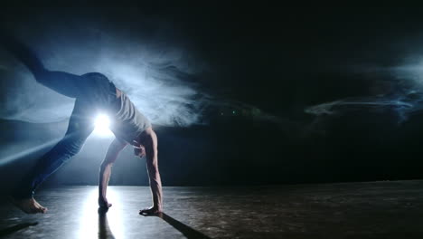 Male-dancer-performs-a-stunt-jump-with-a-rotation-back-and-a-revolution-in-the-scene-in-the-smoke-in-the-spotlight.-Modern-ballet