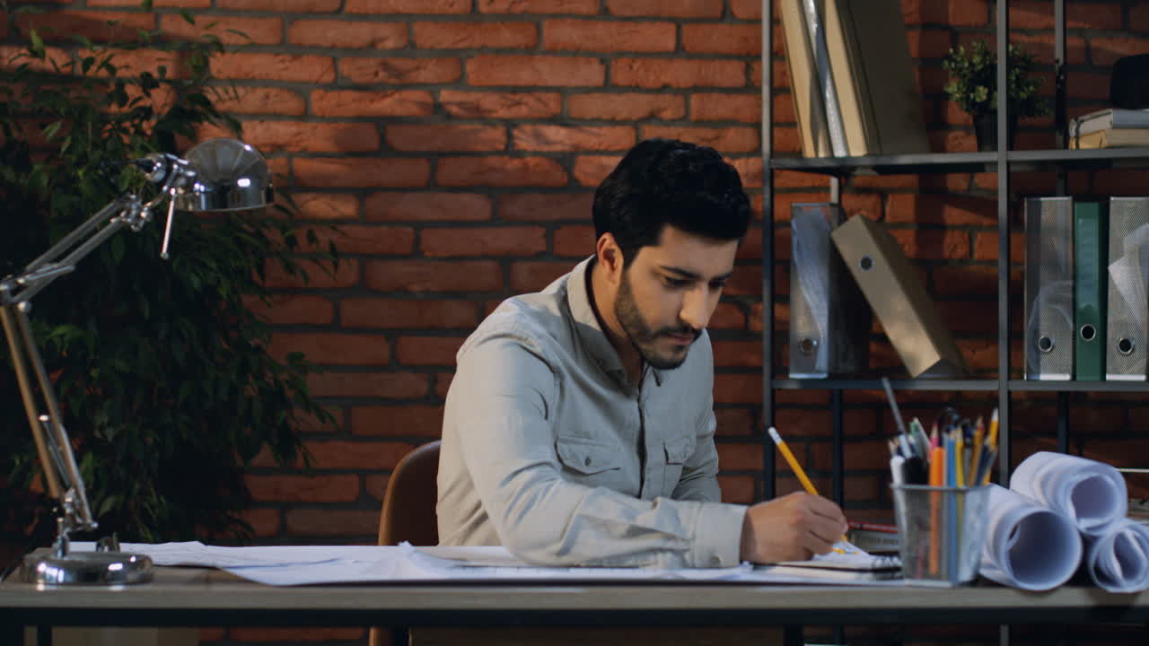 Male Arabian Architect Drawing Some Plan Of New Project And Reading A Design Magazine In The Office