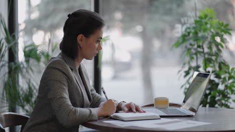businesswoman analyzing the graph and typing on laptop. remote job young female in eyeglasses writes notes in clipboard and typing on laptop keyboard