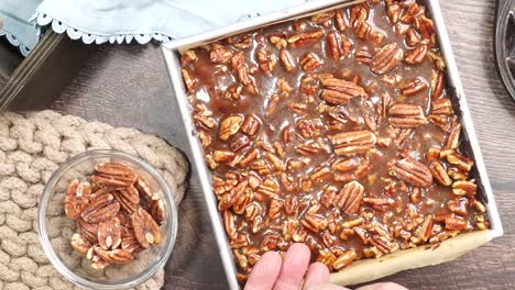 baking delicious caramel pecan brownies. using hands to pick up pecan or nuts to place on top of the caramel topping.. freshly baked gooey chocolate brownies with sweet caramel and nutty pecans.