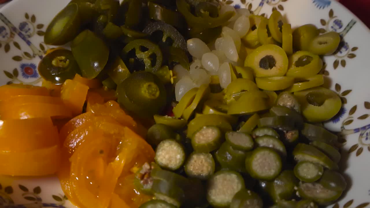Close up view gliding over freshly cut and sliced tomatoes, jalapenos, capars and olives in a artsy bowl on a home kitchen table, pizza toppings