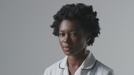 studio portrait of serious female nurse in uniform turning to face camera against plain background