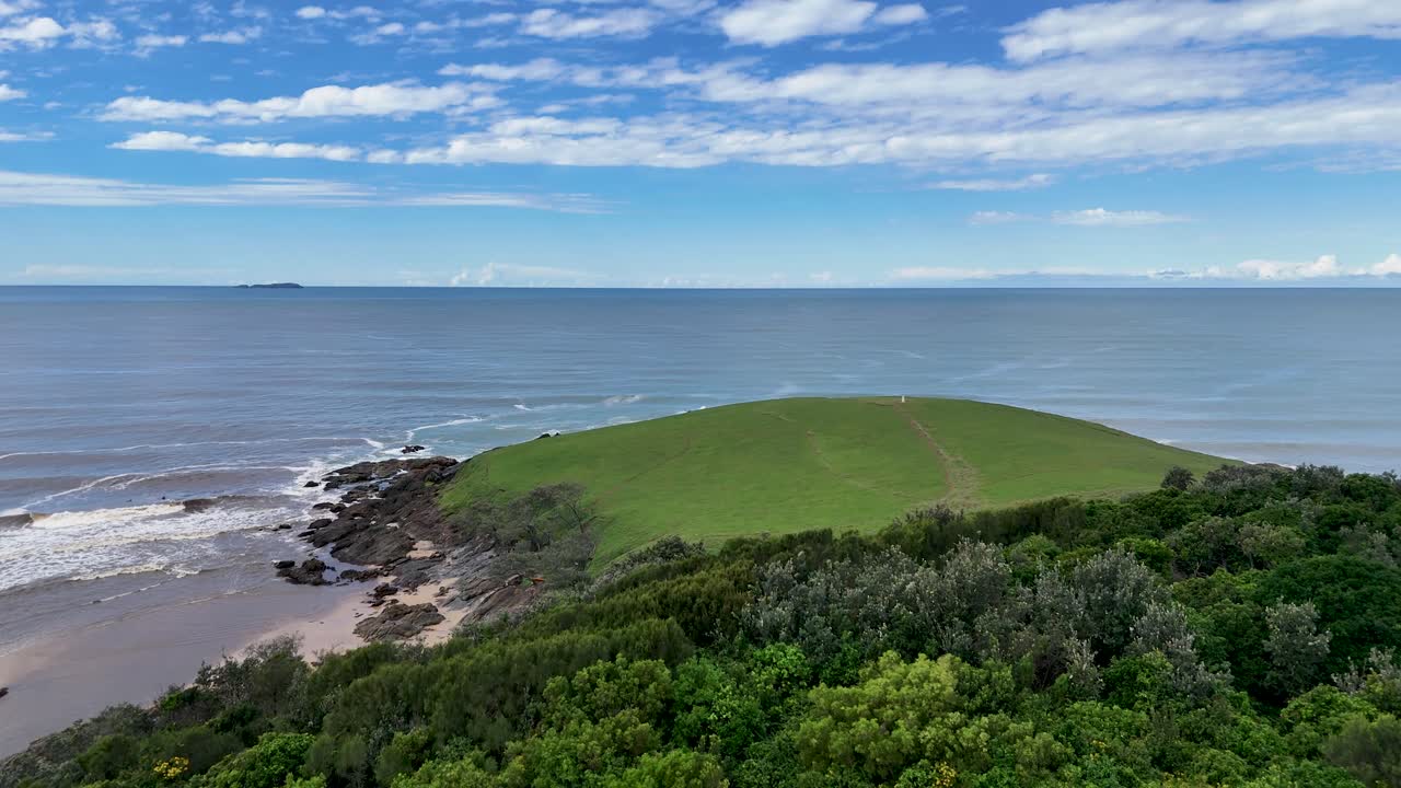 Drone flies over lush coastal headland, revealing ocean views and dramatic shoreline under daylight