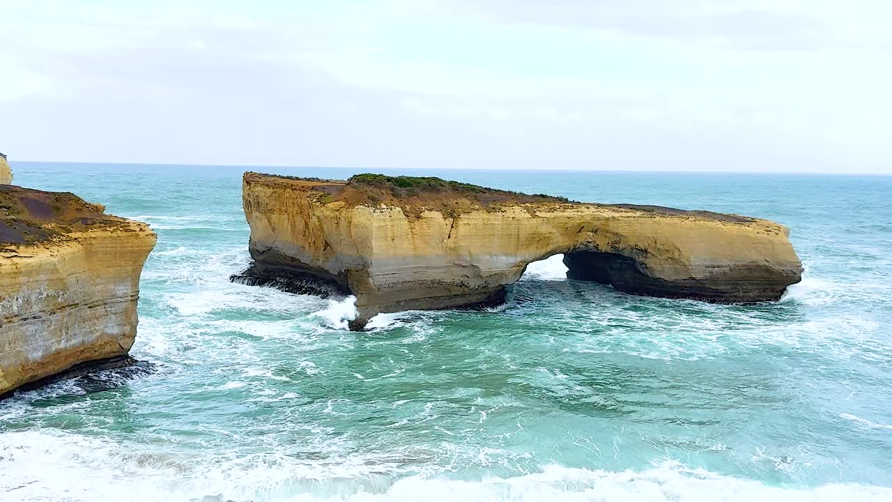 Dynamic ocean waves crash against rugged cliffs at Port Campbell, Australia, under soft daylight, creating a serene yet powerful coastal scene