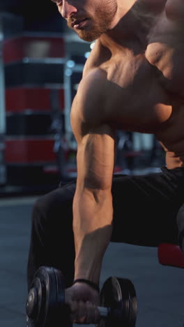 handsome guy with athletic body exercising with dumbbell. shirtless sportsman pumping biceps with heavy weight in the gym. vertical video