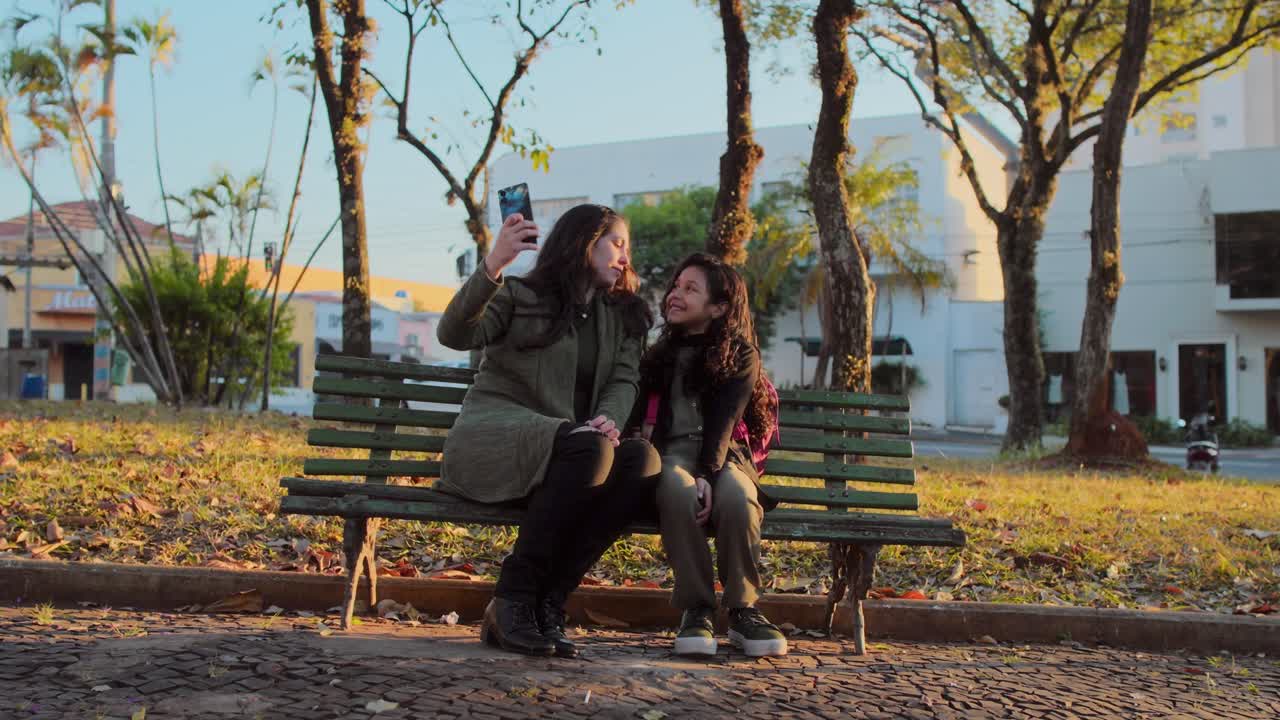 Madre e hija tomándose una selfie en un banco del parque