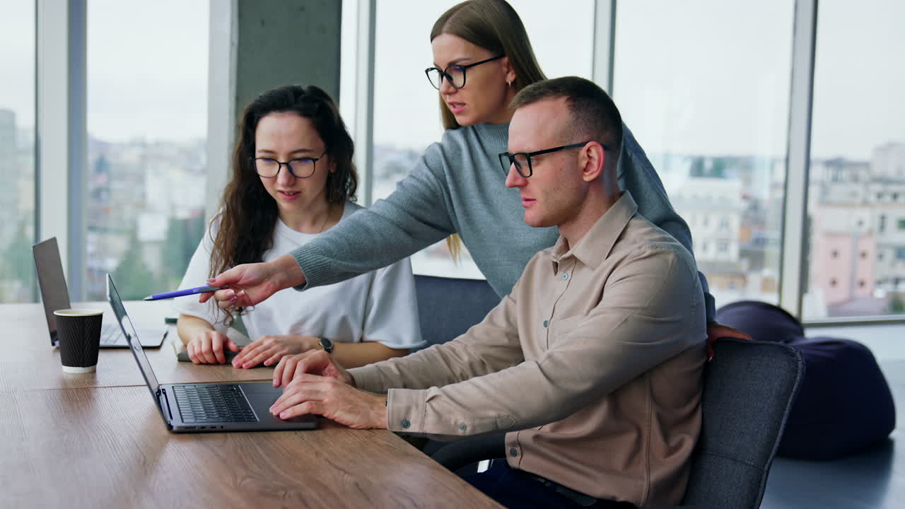 Man shows his female colleagues files on laptop and they actively discuss it. Collaboration on a project.
