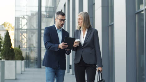 businessman showing project and new ideas on tablet device to woman boss while walking in the street