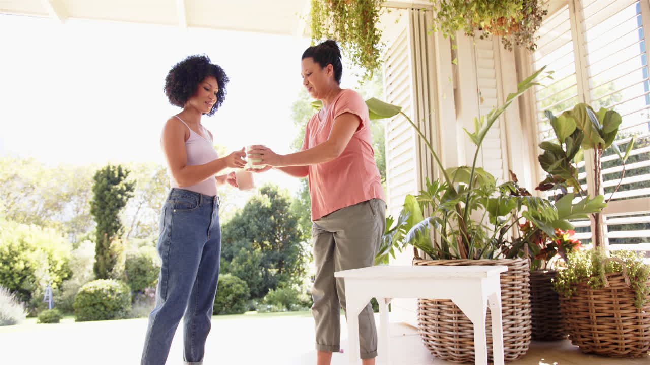 mother and adult daughter exchanging plant care tips on sunny porch with greenery