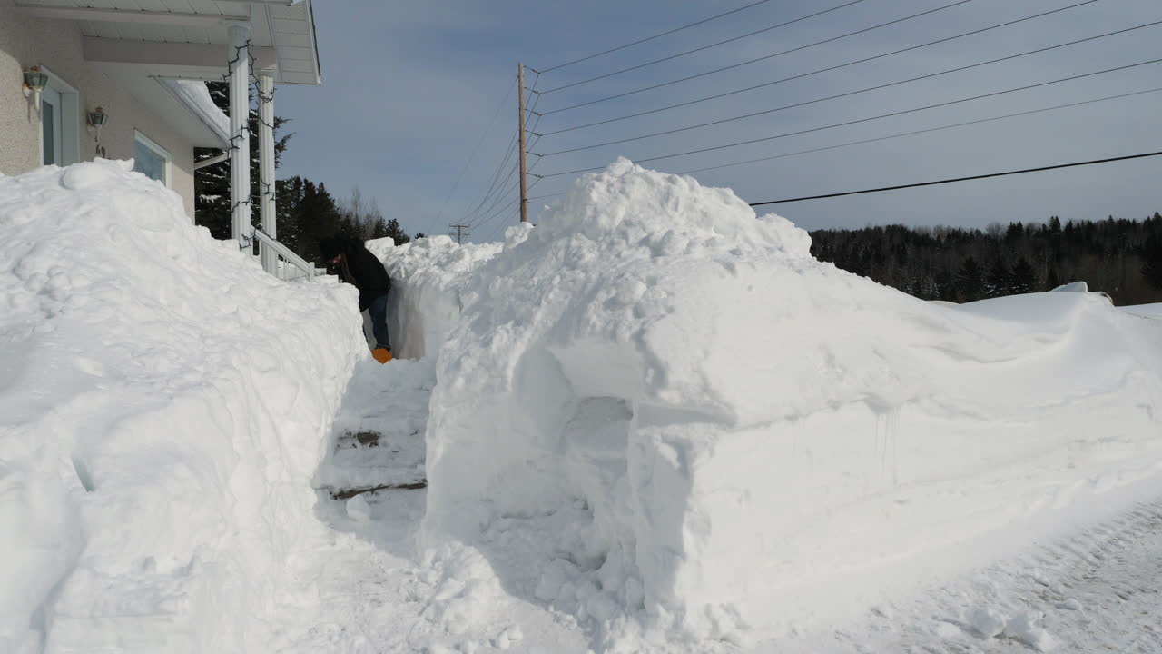 hombre quitando mucha nieve de la pasarela frente a la casa cubierta de nieve