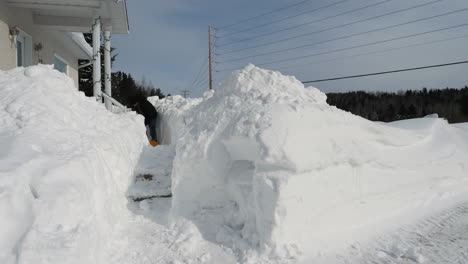 man shoveling a lot of snow off walkway in front of snowbound house