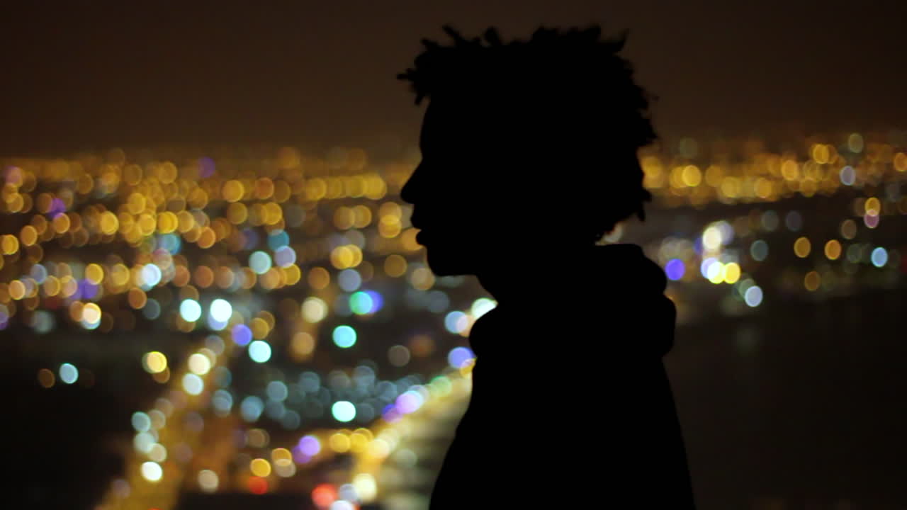 Silhouette of a young man gazing over vibrant city lights in the peaceful night