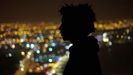 silhouette of a young man gazing over vibrant city lights in the peaceful night