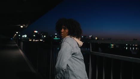 black woman dancing on the bridge at night and looking at camera
