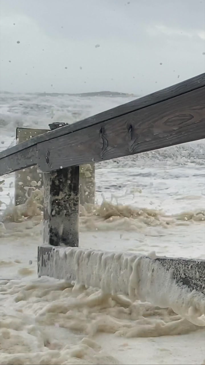 Foamy ocean waves crash against a wooden barrier as a hurricane intensifies. Dramatic scene ideal for depicting severe weather or climate impact.