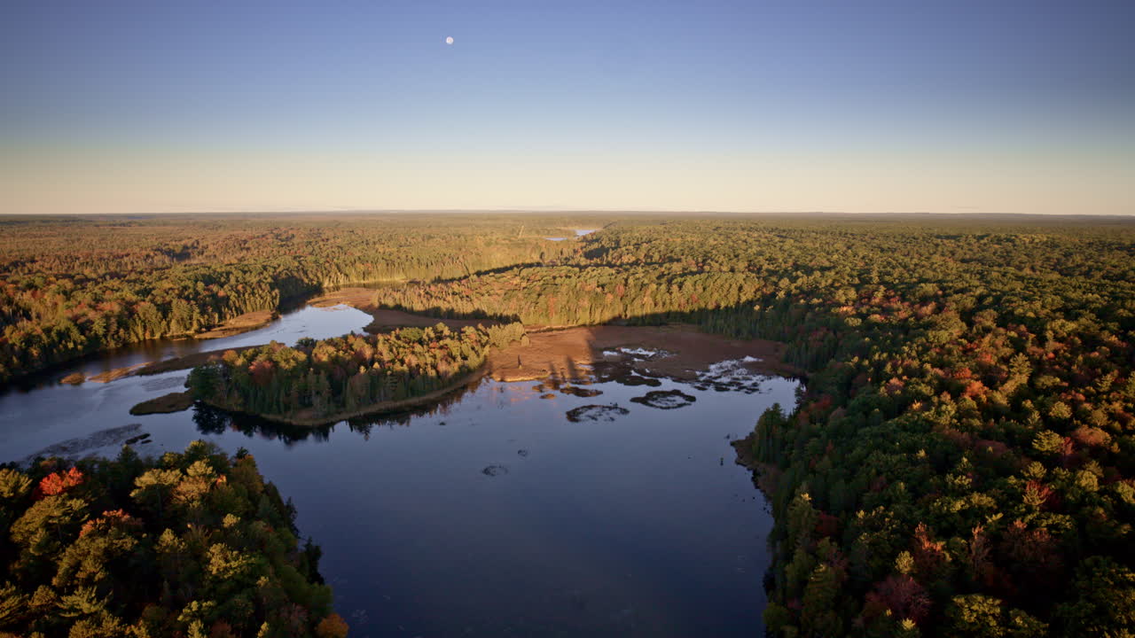 Drone perspective on a river cutting through a broad autumn forest