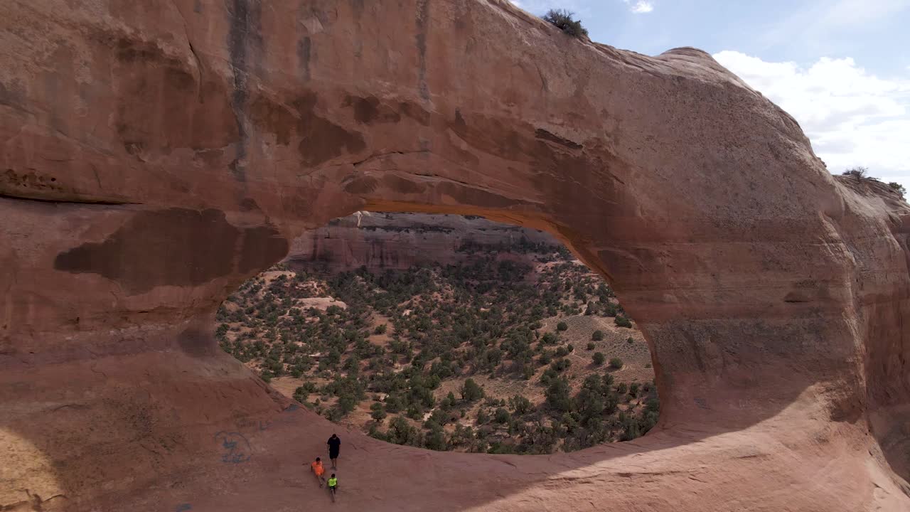 여름에 미국 유타 주 모압에 있는 바위에 앉아 있는 사람들과 함께 윌슨 아치의 무성한 식물이 있는 사막 풍경