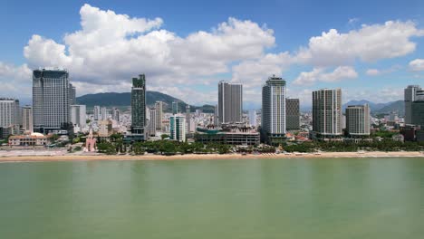 aerial drone view of the nha trang coastline at low altitude and transitioning to high altitude rising above the white sand beach and tall residential buildings on a sunny day