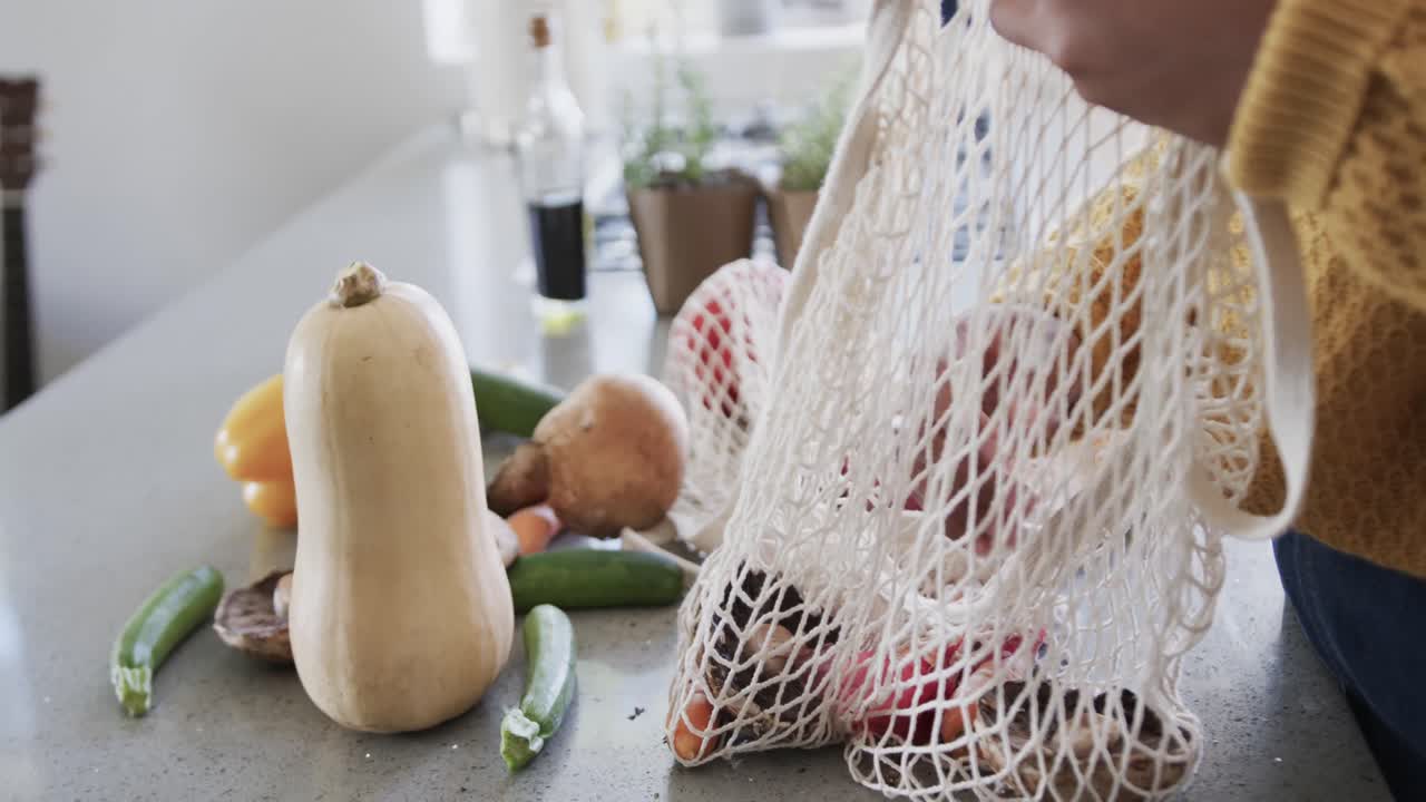 sección media de una mujer afroamericana desempaquetando comestibles en la cocina, en cámara lenta