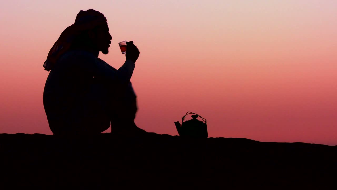 베두인족 남자가 석양을 배경으로 실루엣으로 차를 따른다