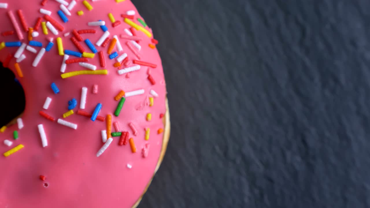 un primer plano de una rosquilla rosada con patatas fritas multicolores y ojos girando lentamente sobre el fondo gris de la mesa.