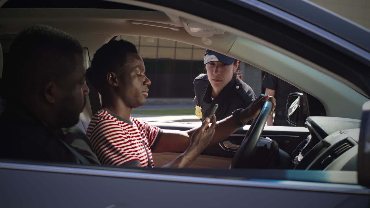 friendly Police Officer Checking Digital License of Black Driver Zoom in View of Positive Woman in Police Uniform Talking with African American Man in Car and Scanning Digital Driver License on Smartphone