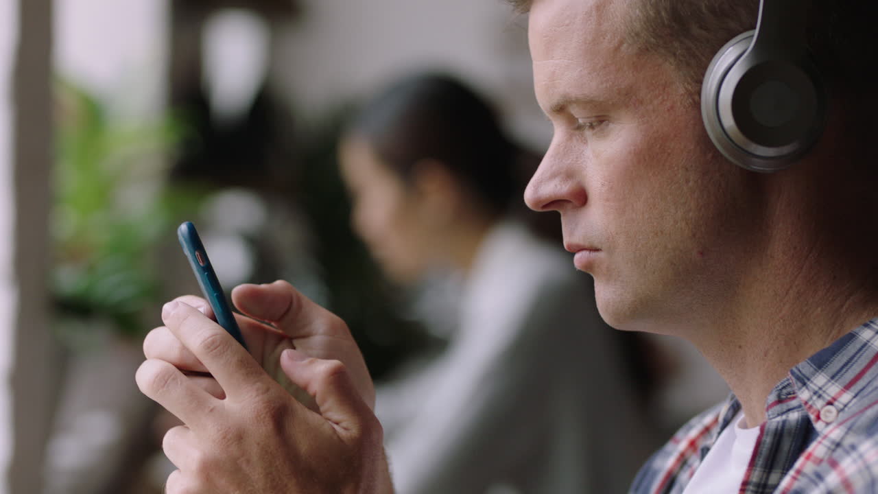 young caucasian man using smartphone in cafe texting typing messages sharing ideas on social media enjoying listening to music wearing headphones